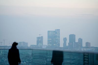 Silhouette man looking at cityscape against sky