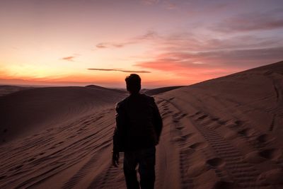 Rear view of silhouette man standing on sand at beach against sky