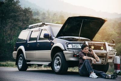 Man sitting by car on road