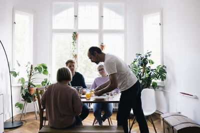 Side view of man serving juice to family on dining table at home