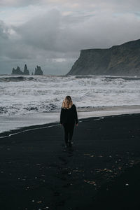 Rear view of woman walking on beach against sky