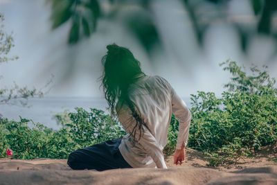 Side view of woman sitting on plant against sky