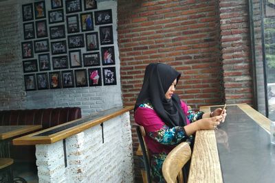 Full length of young woman sitting on brick wall