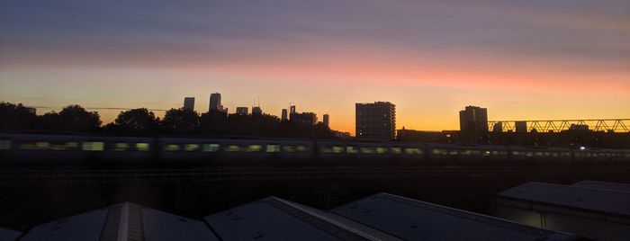 Cityscape by river against sky during sunset