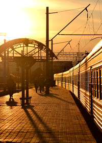 People waiting at railroad station platform against sky during sunset