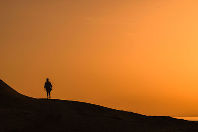 Silhouette man standing on rock against sky during sunset