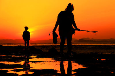 Silhouette men standing on beach against sky during sunset