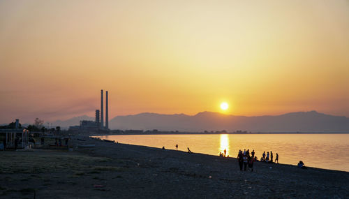 Silhouette people on beach against sky during sunset