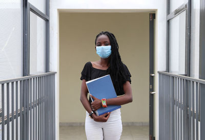 Portrait of young woman wearing mask standing against wall