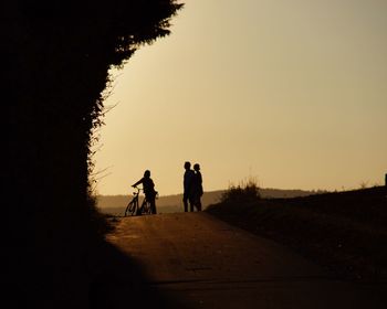 Silhouette of people talking while standing on dirt road against sky during sunset