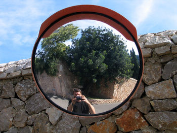 Man with camera reflecting in road mirror on stone wall