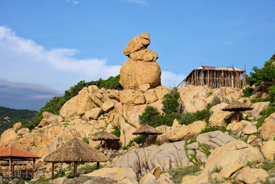 Thatched roof parasols by rock formations against blue sky