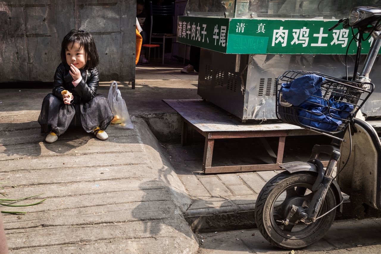 sitting, one person, real people, full length, day, transportation, lifestyles, text, front view, casual clothing, women, mode of transportation, city, container, outdoors, street, communication