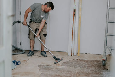 A young man vacuums the floor with a construction vacuum cleaner.