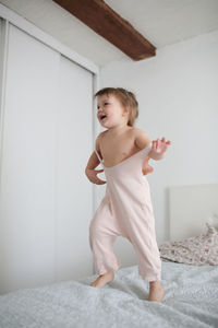 Happy funny girl toddler life style with a smile jumping on the bed, the concept of happy light 