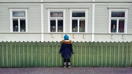 Rear view of girl standing by picket fence looking at house