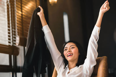 Cheerful businesswoman with arms raised at office