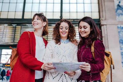 Group of three young caucasian women at train station reading a map. travel and friendship concept