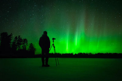 Rear view of silhouette man standing against sky at night with northern lights 