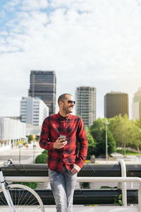 Full length portrait of young man standing in city against sky