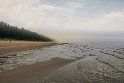 Scenic view of misty tranquil beach against sky