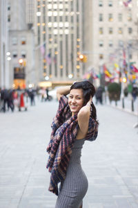 Side view portrait of happy beautiful woman with scarf standing on street in city