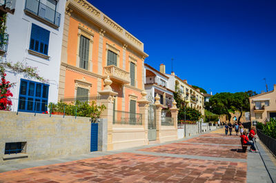 People walking on street amidst buildings against blue sky