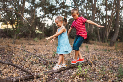 Full length of boy and girl walking on fallen tree