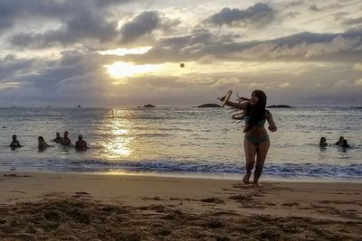 People standing on beach against sky during sunset