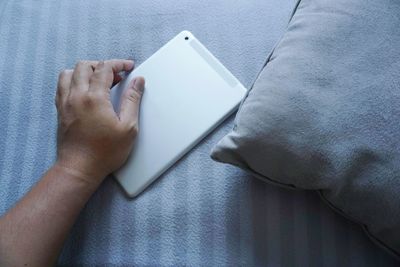Cropped hand of man by digital tablet on bed