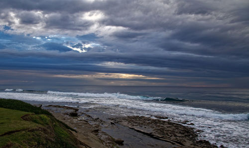 Scenic view of beach against cloudy sky during sunset