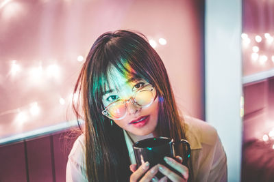 Portrait of young woman having coffee at illuminated home