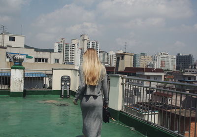 Rear view of woman standing by buildings against sky