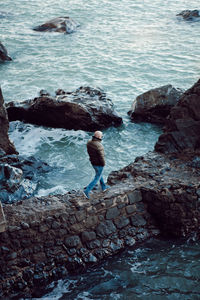 A man walks on huge boulders near the seashore