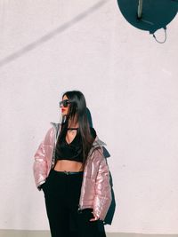 Young woman wearing sunglasses standing against wall