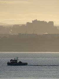 Scenic view of small fishing boat traveling across a backdrop of the edinburgh skyline 