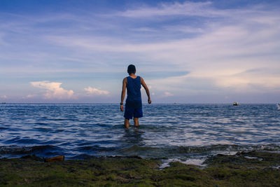 Rear view of man standing on sea against cloudy sky