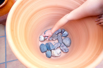 A person's arm deposits stones at the bottom of a large flower pot.