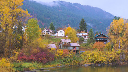 Houses and trees by lake in forest during autumn