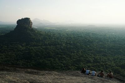 Rear view of friends sitting on cliff against sky