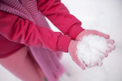 Woman in pink clothes gloves pants jacket holds snow in her hands