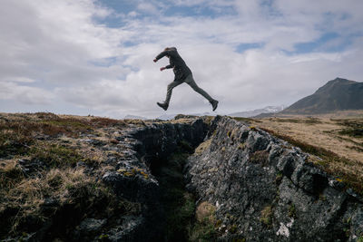 Side view of man jumping on rock against sky