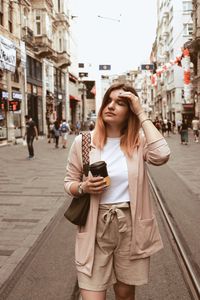 Young woman with disposable cup standing on street in city