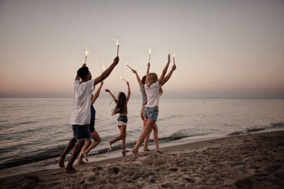 Rear view of people on beach against sky during sunset