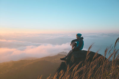 Man standing on rock against cloudscape during sunset