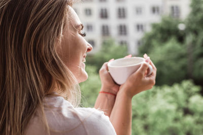 Beautiful young woman on a balcony enjoing morning with cup of tea