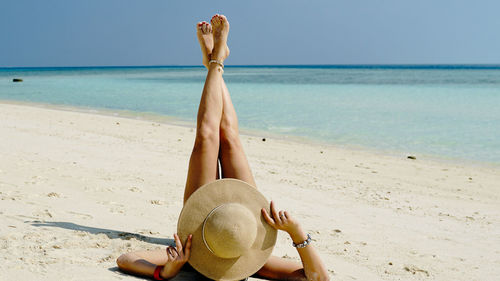Rear view of woman relaxing at beach against sky