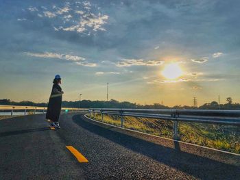 Rear view of woman on road against sky during sunset