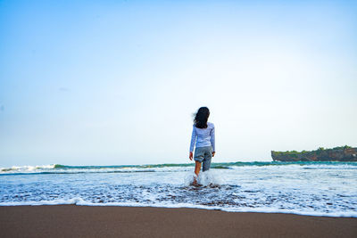 Rear view of woman standing on beach against clear sky