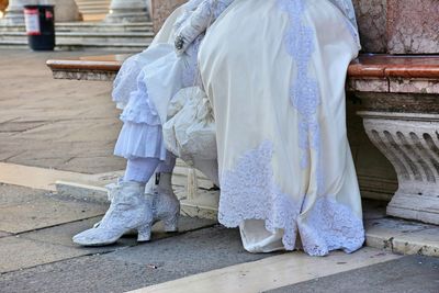 Low section of woman wearing dress sitting on retaining wall in city